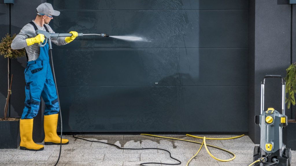 A man cleans his garage door, using one of the three fall maintenance tips for garage doors